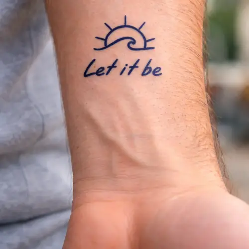 tatouage-semi-permanent-soleil-vague-tattoo-jagua-mikiti Tatouage semi-permanent au jagua, représentant une vague stylisée avec un petit soleil et la phrase « Let it be ». Le tatouage est de couleur bleu nuit profond, minimaliste, discret et réaliste, conçu pour durer 8 à 15 jours.